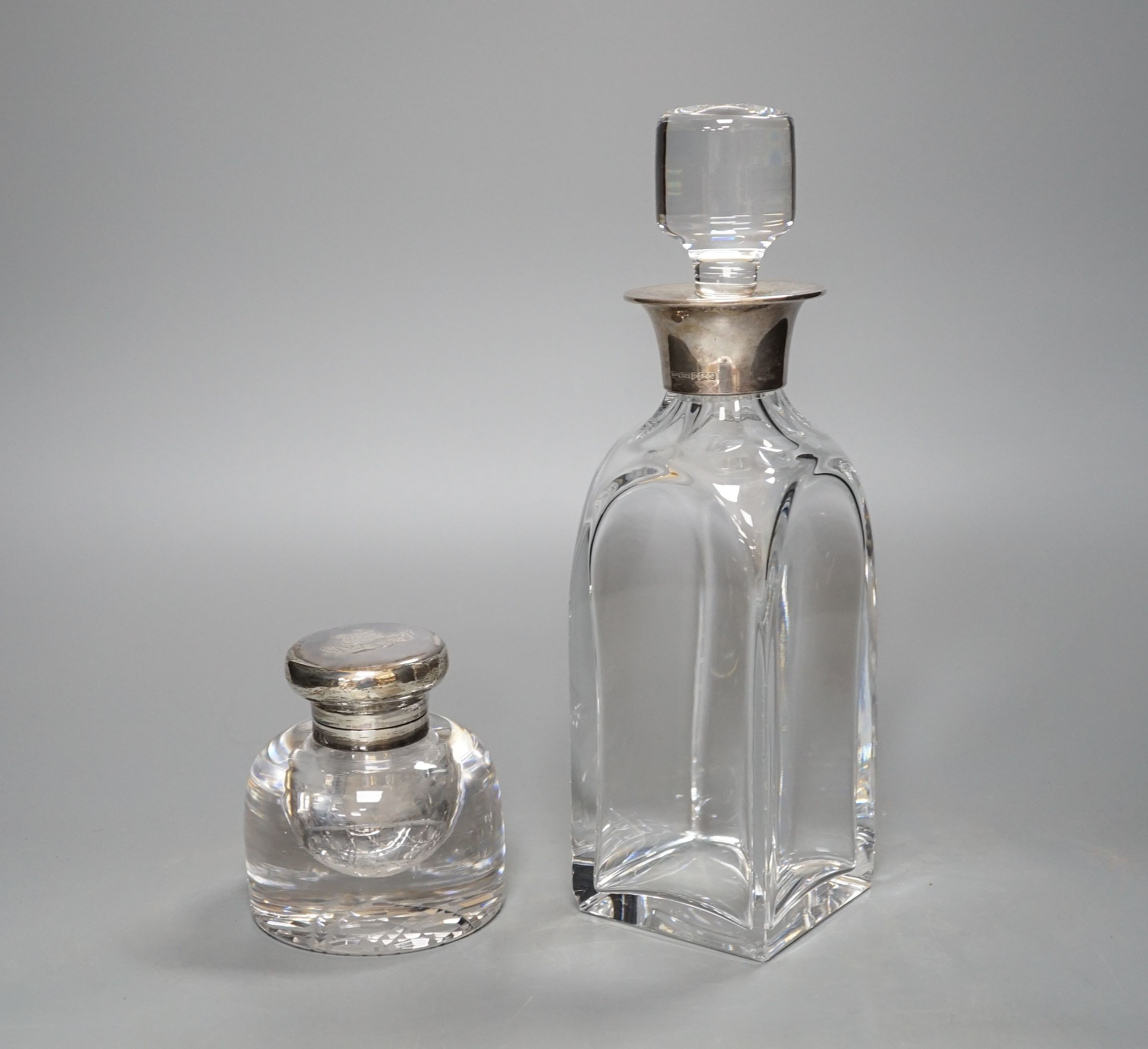 A Victorian circular heavy glass inkwell with hinged silver lid, engraved crest (London 1892) and a silver mounted decanter, 26.5cm